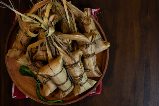 Top view of traditional lepet wrapped in coconut leaves on wooden plate, Indonesian sticky rice dish ideal for festive, cultural, and authentic Asian food themes.