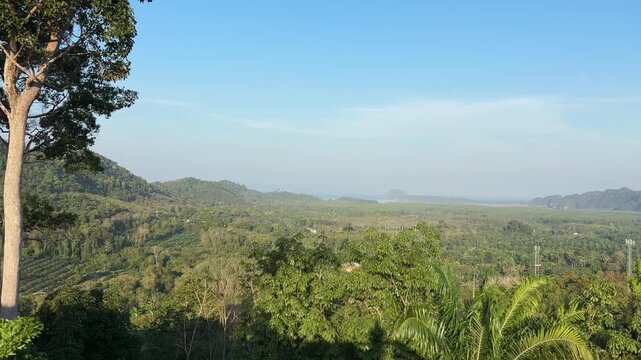 Wide view over green valley and distant coastline at sunrise from Din Daeng Doi in Krabi Thailand showing tropical forest, soft haze, and peaceful natural landscape