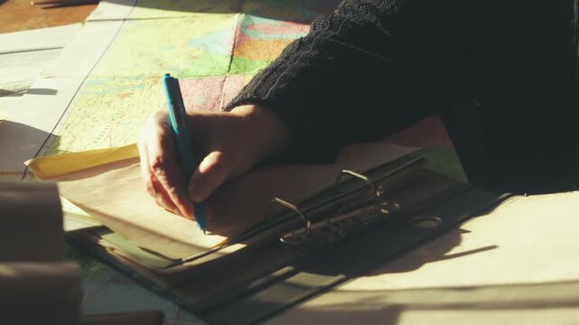 Sunlit shot of a person transferring information from a colorful vintage road map into a clip binder folder. Perfect for travel planning.