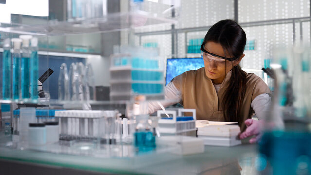 Female scientist in protective gear working in a laboratory to test human DNA samples. Preparing test samples for examination with a pipette. Selective focus