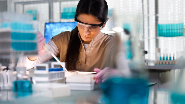 Female scientist in protective gear working in a modern laboratory to DNA samples. Preparing test samples for examination with a pipette. Selective focus