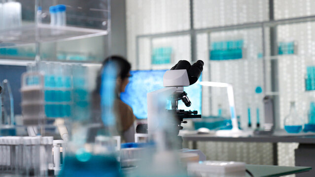Female scientist in protective gear working in a modern laboratory to test human DNA samples. Taking notes on a computer. Selective focus