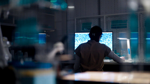 Female scientist in protective gear working in a modern laboratory to test human DNA samples. Working on a computer in the dark