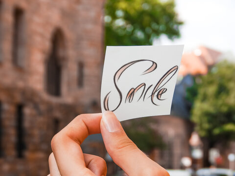 Hand holding paper note with smile text against the background of the Imperial Castle in Poznań