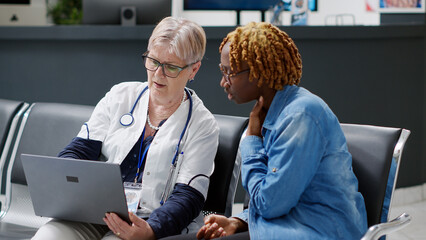 Senior physician showing disease diagnosis to young woman on laptop, explaining treatment at...