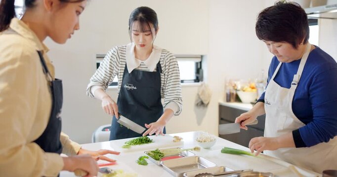 Cooking class, women and chopping to cook, chef and japanese food in kitchen, professional and skill. Restaurant, teaching and course for culinary skills, working together and aprons for cleanliness