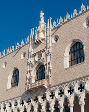 View of the ornate Doge's Palace facade, showcasing intricate stonework and gothic arches against a clear blue sky, Venice, Veneto, Italy.