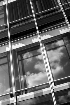 Monochrome glass building facade with windows reflection of clouds and high contrast geometry creating abstract modern urban architecture background