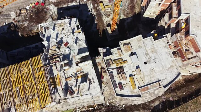 Workers are busy at a construction site where several concrete structures are being built. Equipment is present along with materials scattered around the site in a developing area.