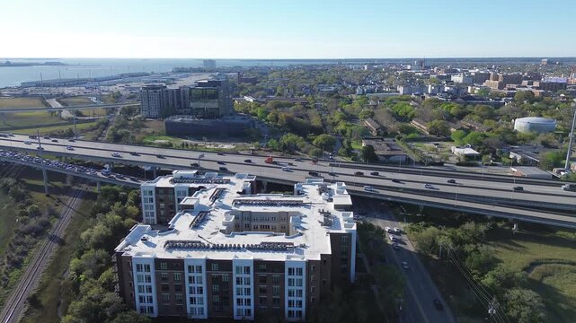 Meeting St and Morrison Dr corridors run beside elevated highway lanes and parallel rail tracks in Charleston Upper Peninsula. Warm light over rooftops, tree canopies, metallic roadway textures