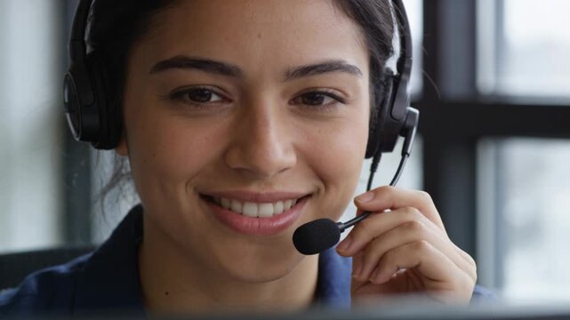 Smiling woman in blue polo adjusting headset mic, speaking at office desk during incoming call