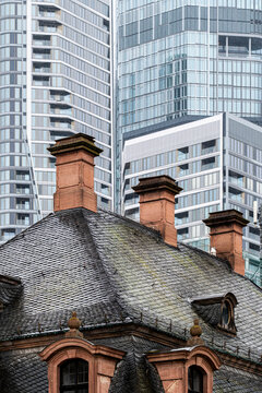 Architecture contrast in Frankfurt Bankenviertel Germany where historic facade meets modern skyscraper skyline above rooftop chimneys