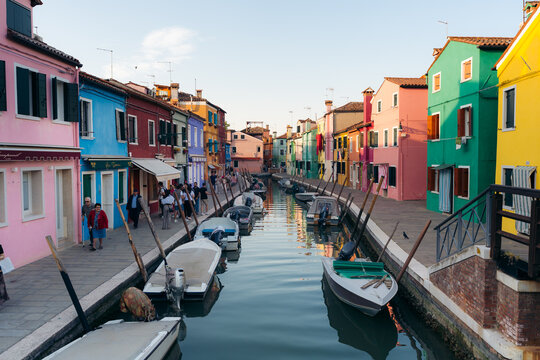 View of vibrant houses cast reflections on the still canal waters where boats are moored, a picturesque scene in Burano, Venice, Italy.