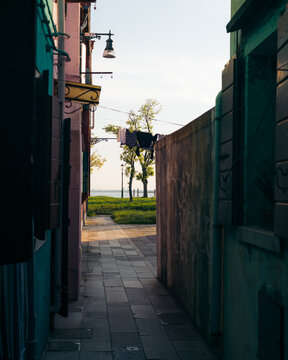 View of a narrow alleyway framed by vibrant buildings leads to a distant glimpse of the sea in the colorful tapestry of Burano, Venice, Italy.