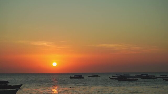 Stunning golden sunset over Stone Town beach in Zanzibar. Traditional dhow boats anchored in the calm Indian Ocean under a vibrant orange and yellow sky at dusk