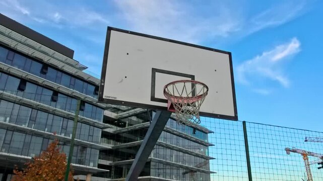 Sofia, Bulgaria - 10.31.2025: Outdoor basketball court with hoop and backboard at Garitage Park business district, modern office buildings and urban architecture in the background