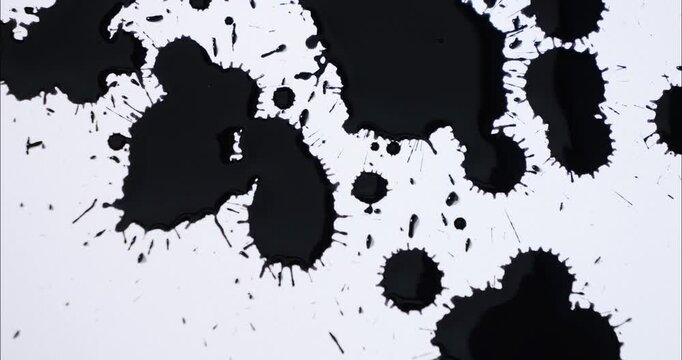 Black spots on a white background. Ink spills onto white paper. Black drops and white surface.