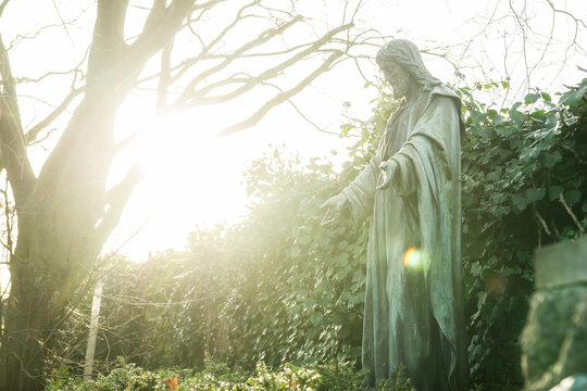 Statue von Jesus auf einem Friedhof im Gegenlicht, Konzept Glaube und Tod 