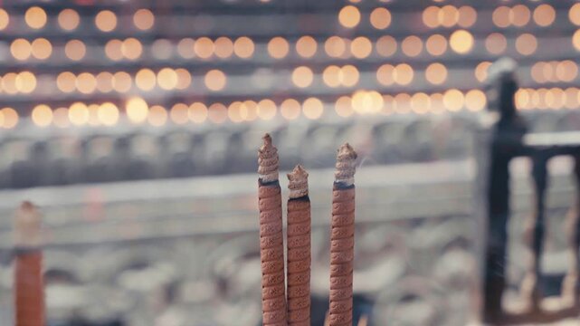 Extreme close-up static shot of three decorated burning incense sticks with curled ash tips against a warm golden bokeh light background at Luohan Temple in Chongqing, serene and meditative atmosphere