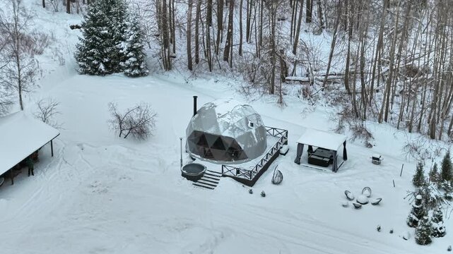 Domed igloo houses or glamping accomodation in snow covered forest scene, drone view