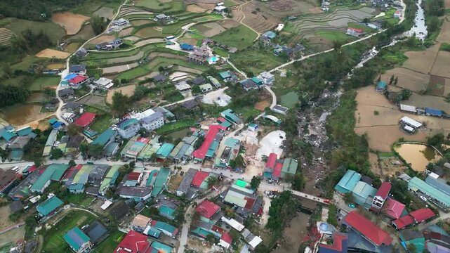 Overhead drone view captures a small town in a mountain valley with riverside houses agricultural land and roads following a winding river through a green countryside landscape