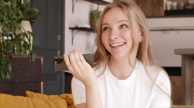 Smiling young woman recording voice message, dictates thoughts. Blonde lady record voice answer in social network audio messages using phone