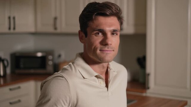 Smiling man responding to camera gaze, forming gentle closed grin in kitchen, with microwave