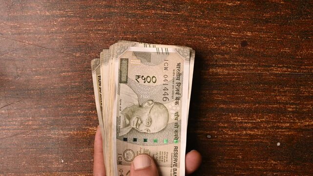 Top View of Man Placing 500 Rupee Note Bundles on Wooden Table &ndash; Financial Concept