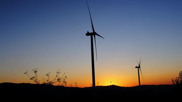 Dark silhouettes of rotating wind turbines in evening field under clear sky slow motion. Sustainable electric power generation station