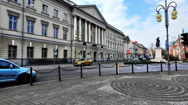 Historic District Court building in Kalisz, neoclassical architecture with columns, square with Jozef Pilsudski monument, city street and panorama of the historic town center on a sunny day.