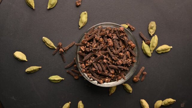 Top View of Cloves (Laung) in White Bowl Cardamom (Elechi) on Black Background &ndash; Rotating Footage