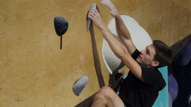 Strong man balances on wall clinging to hook slow motion. Competitor confidently heading along wall reaching final of course