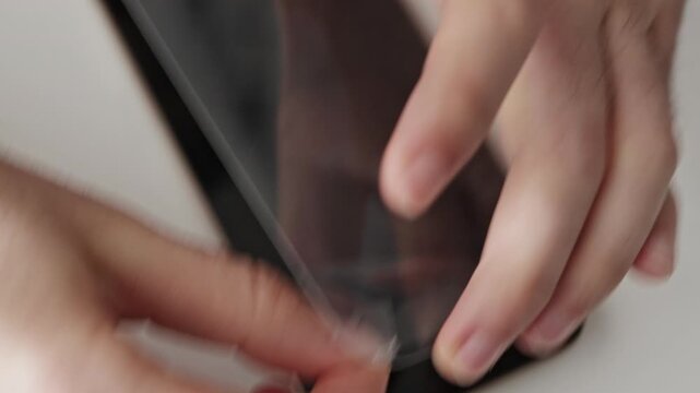 Man replaces cracked glass on phone screen at home. Hand removes broken glass, unpacks wipe, cleans dust and uses tools to install new glass. Repair process, close view, device maintenance.