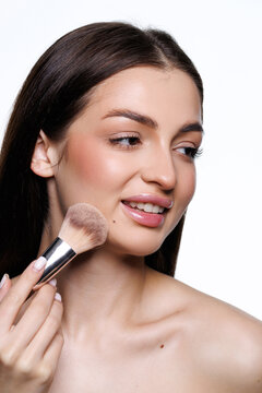 Young pretty woman applying blush with a brush in a minimalistic setting during daylight