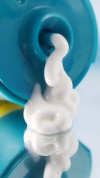 Close up of white cream slowly dispensing from turquoise packaging, skincare product with smooth texture on clean background.
