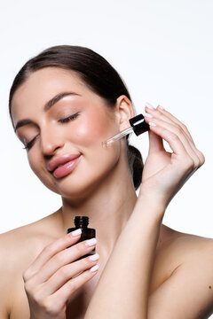 Close-up young female applying facial serum, using anti-aging treatment product, hydrating and nourishing skin on white background