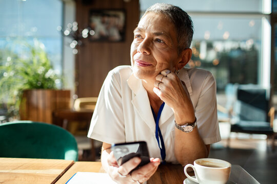 Mature woman with smartphone daydreaming in cafe
