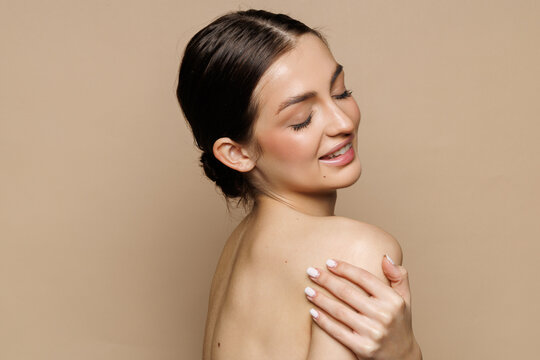 Skin care model. Beautiful young woman with perfect skin touching her face and posing against beige background.
