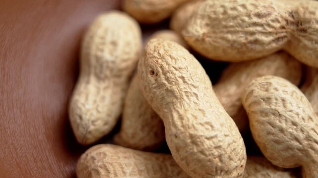 Whole peanuts in shell inside kitchen bowl. Natural snack food. Roasted nuts with dry texture. Top view. Rotation