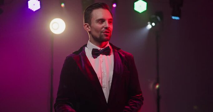 Presenter host emcee on stage under lights. Charismatic showman performer gestures amid spotlight and concert lights, engaging crowd. Strong concept of hosting energy and entertainment.