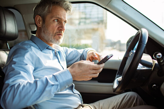 Mature man using smartphone while driving in car