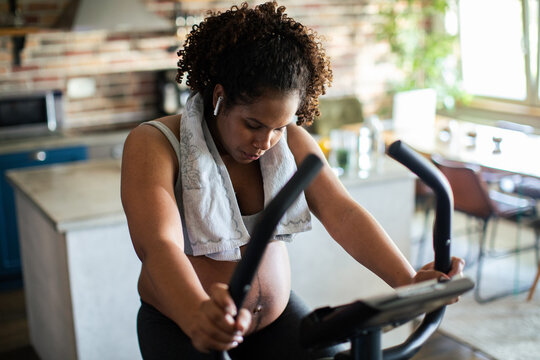 Pregnant woman cycling on an exercise bike in a home kitchen