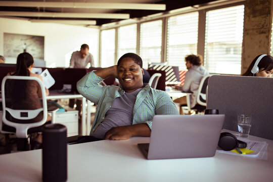 Smiling man relaxing at laptop in modern open office