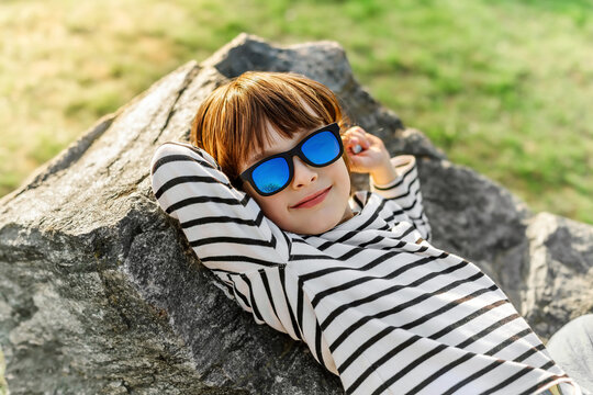 Happy boy in sunglasses relaxing on rock outdoors on sunny summer day