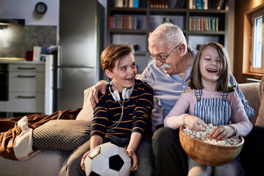 Grandfather and grandchildren sharing popcorn on sofa at home