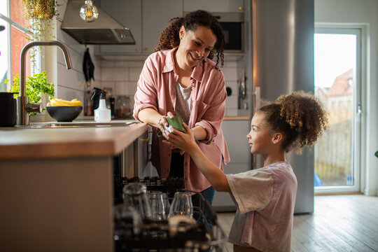 Mother and daughter unloading dishwasher in home kitchen