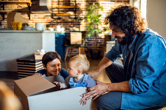 Father and children playing with moving box in modern home kitchen