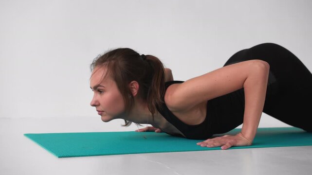 Flexible young woman performing the bhujangasana or cobra pose during a yoga session. Slow motion footage on a white background