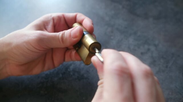 Male hands holding a door lock cylinder and a key, demonstrating how the mechanism works by inserting and turning the key to show the pins and tumblers inside the core moving