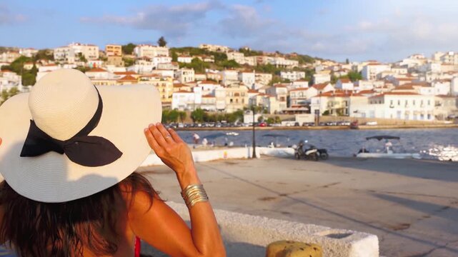 A tourist woman in a red dress  on summer vacations looks at the cityscape of Pylos, Messinia, Greece, during sunset time
